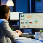 Busy woman working at night in front of computer taking notes