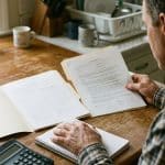 Personal Loan Origination Fees: Calculate Your Net Proceeds An adult compares paperwork beside a calculator at a kitchen table.
